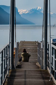 Serene pier with people overlooking mountains and calm water.
