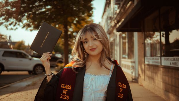 Young woman in graduation attire holding diploma, Class of 2025.