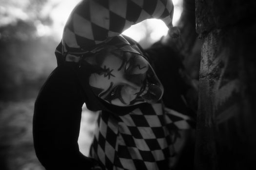 Eerie black and white portrait of a harlequin character in unsettling makeup outdoors.