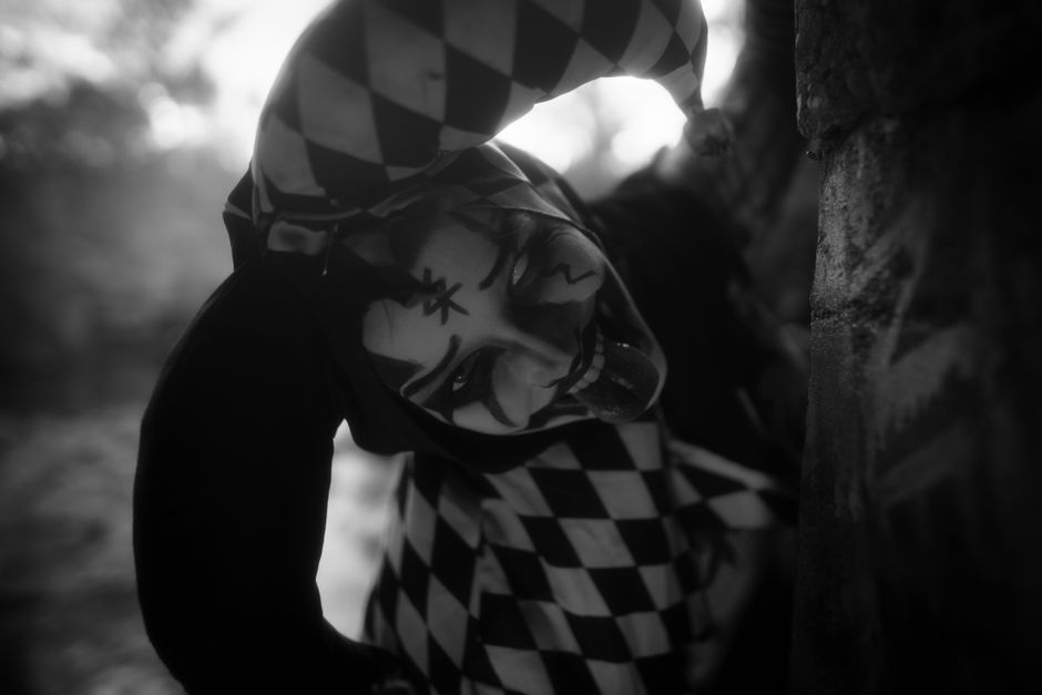 Eerie black and white portrait of a harlequin character in unsettling makeup outdoors.