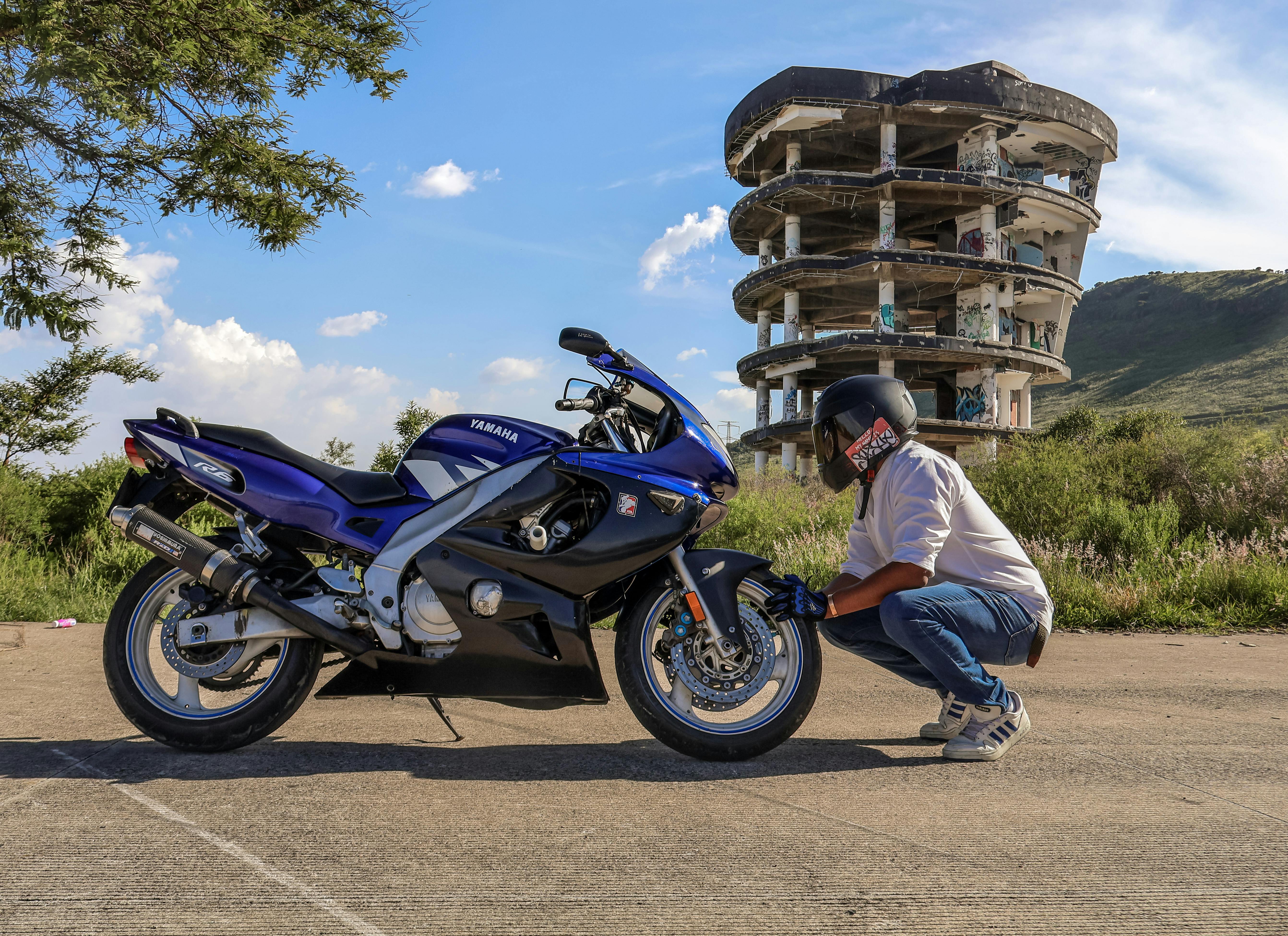 Man adjusts motorcycle near abandoned building on sunny day.