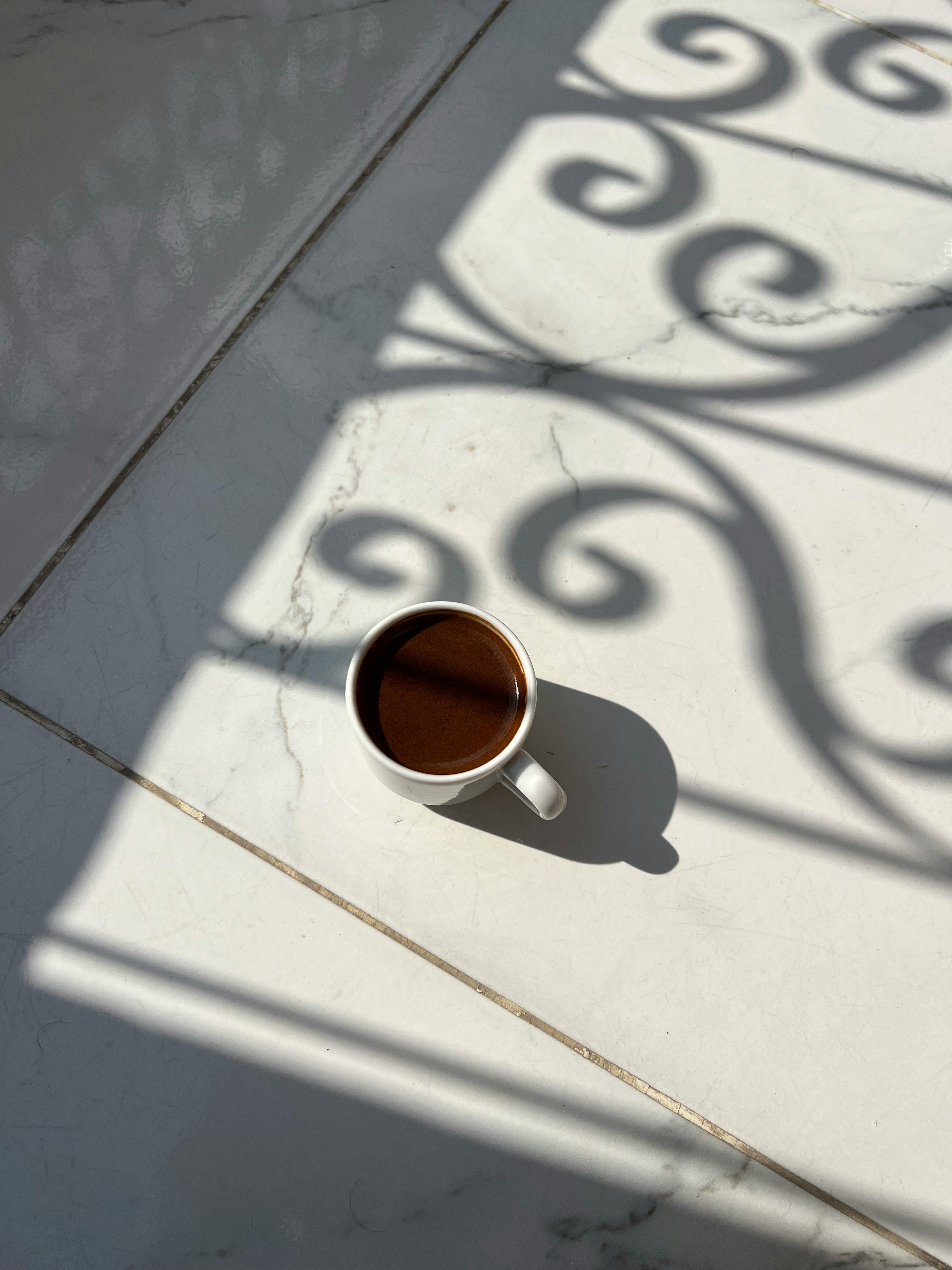 A white coffee cup casts a shadow on a sunlit marble floor, evoking calm mornings.