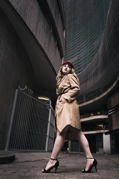 Stylish woman in a trench coat poses in an urban setting with retro flair.