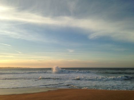Peaceful sunrise over the ocean with gentle waves crashing on the sandy beach.