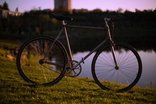 A solitary bicycle stands beside a peaceful lake at sunset, casting a reflective silhouette.