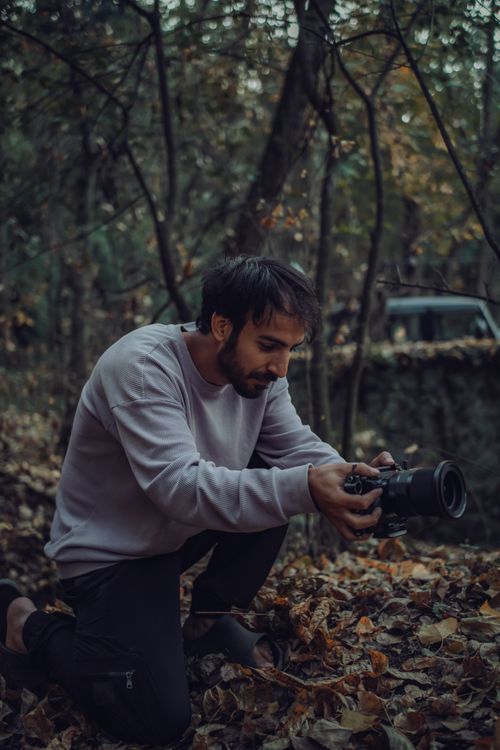 Free A photographer kneels in a forest capturing a scenic autumn landscape. Stock Photo