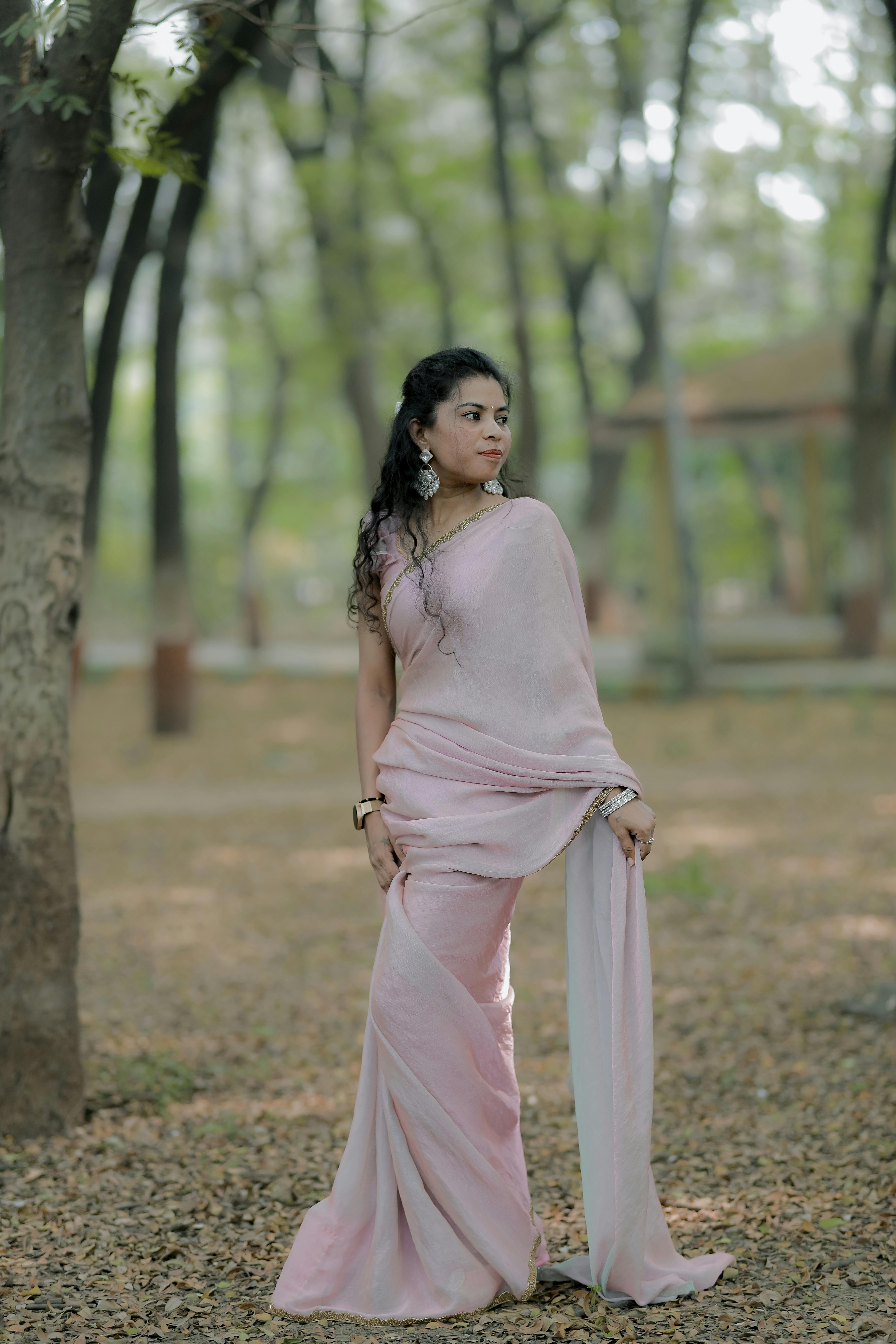 Free Graceful woman in a pink sari standing in a serene forest setting, showcasing traditional fashion and elegance. Stock Photo