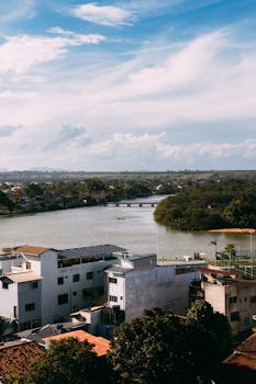 A picturesque view of a riverside cityscape with a clear blue sky and a bridge over the river.