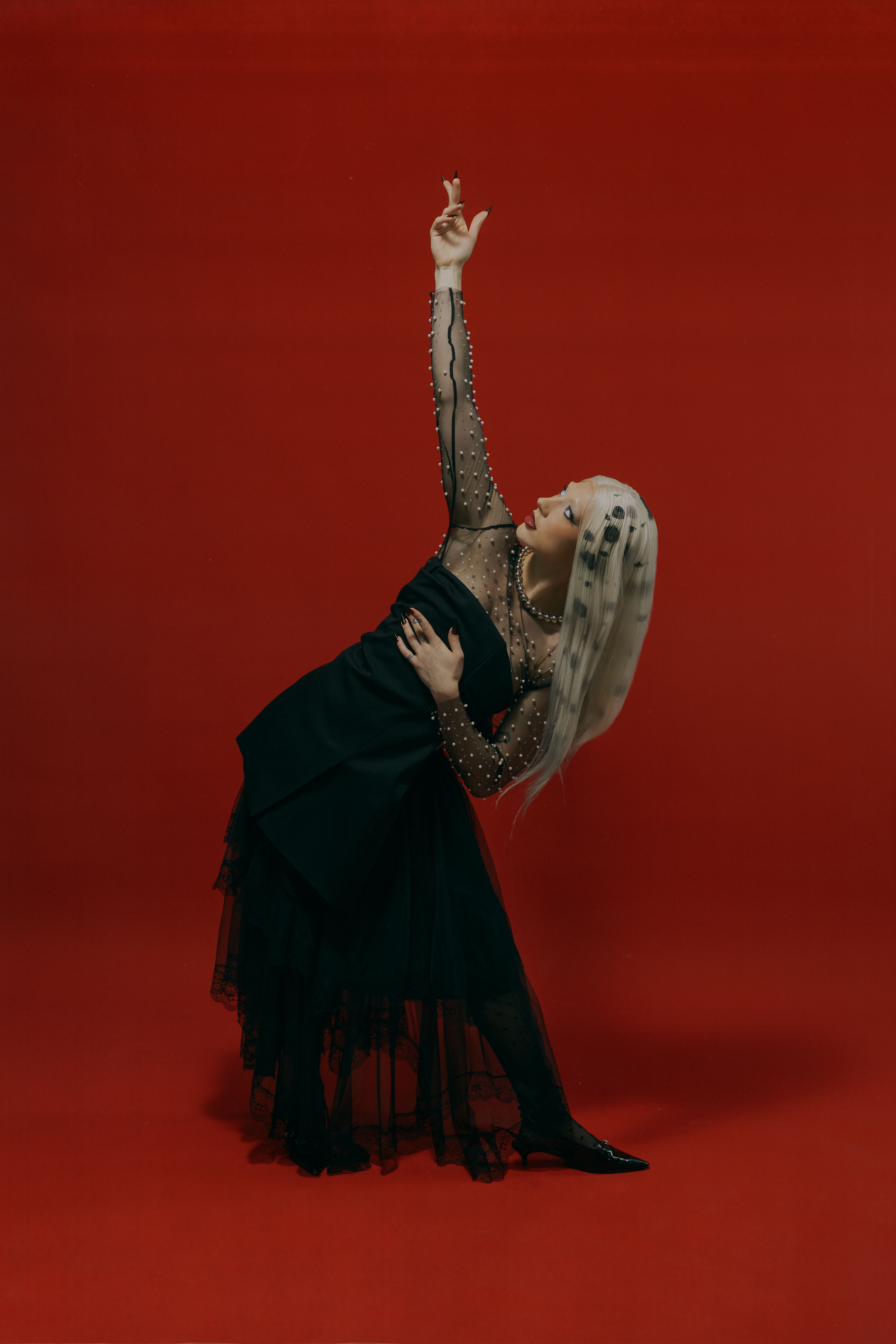 Striking pose by a woman in a black dress against a vibrant red background, capturing elegance.