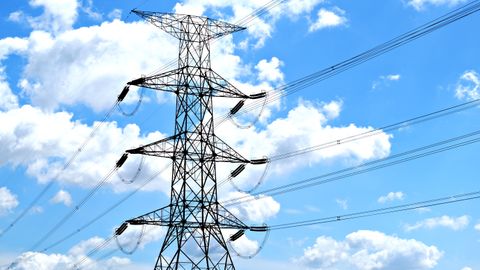 Electricity pylon with high voltage lines set against a vibrant blue sky with clouds.