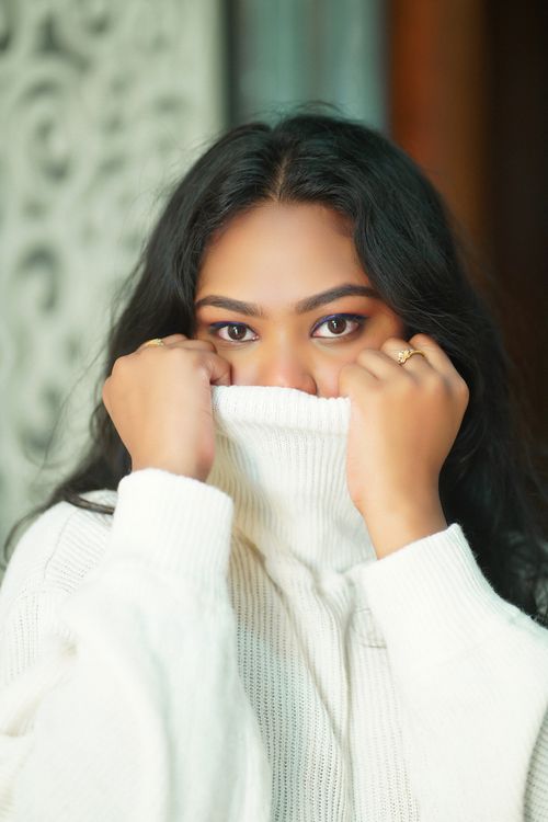Free A woman in a white sweater partially covers her face, exuding mystery and warmth, indoors. Stock Photo