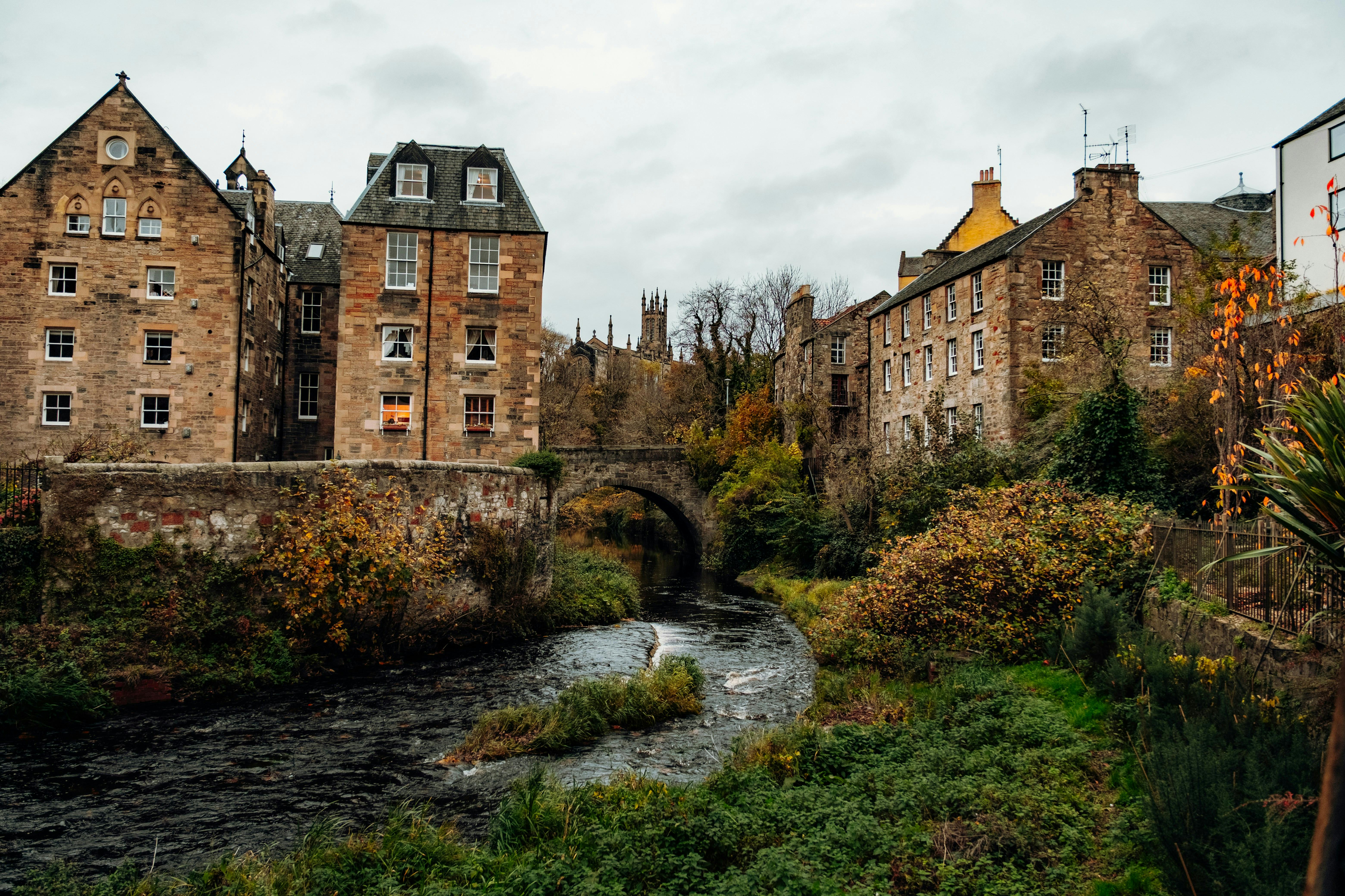 Picturesque autumn view of Edinburgh's historic architecture by a serene stream.