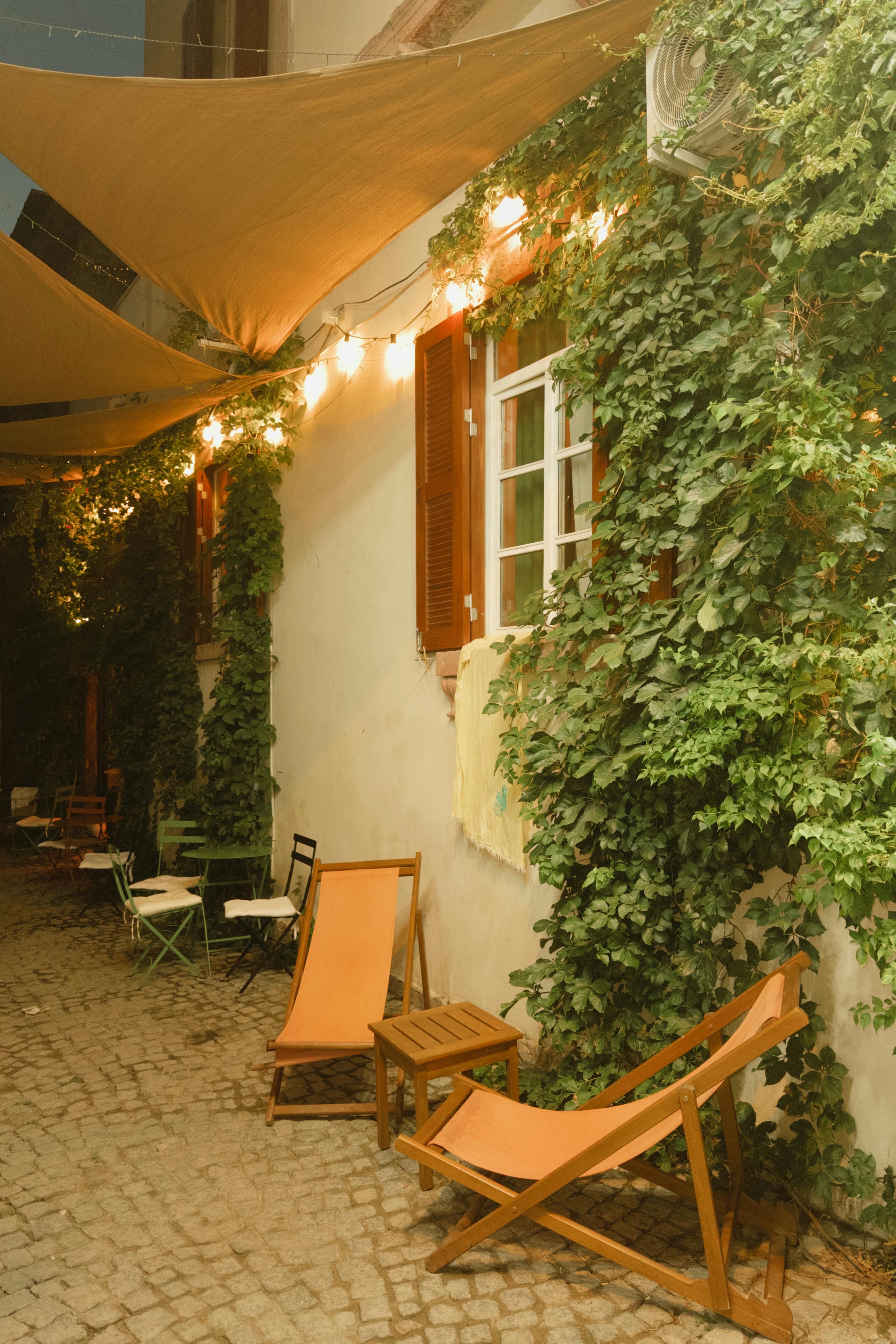 Charming outdoor patio with chairs and climbing plants, warmly lit by string lights at night.
