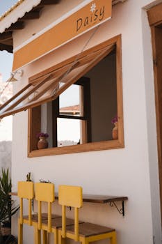 Cozy outdoor café with yellow chairs and open window under 'Daisy' sign.