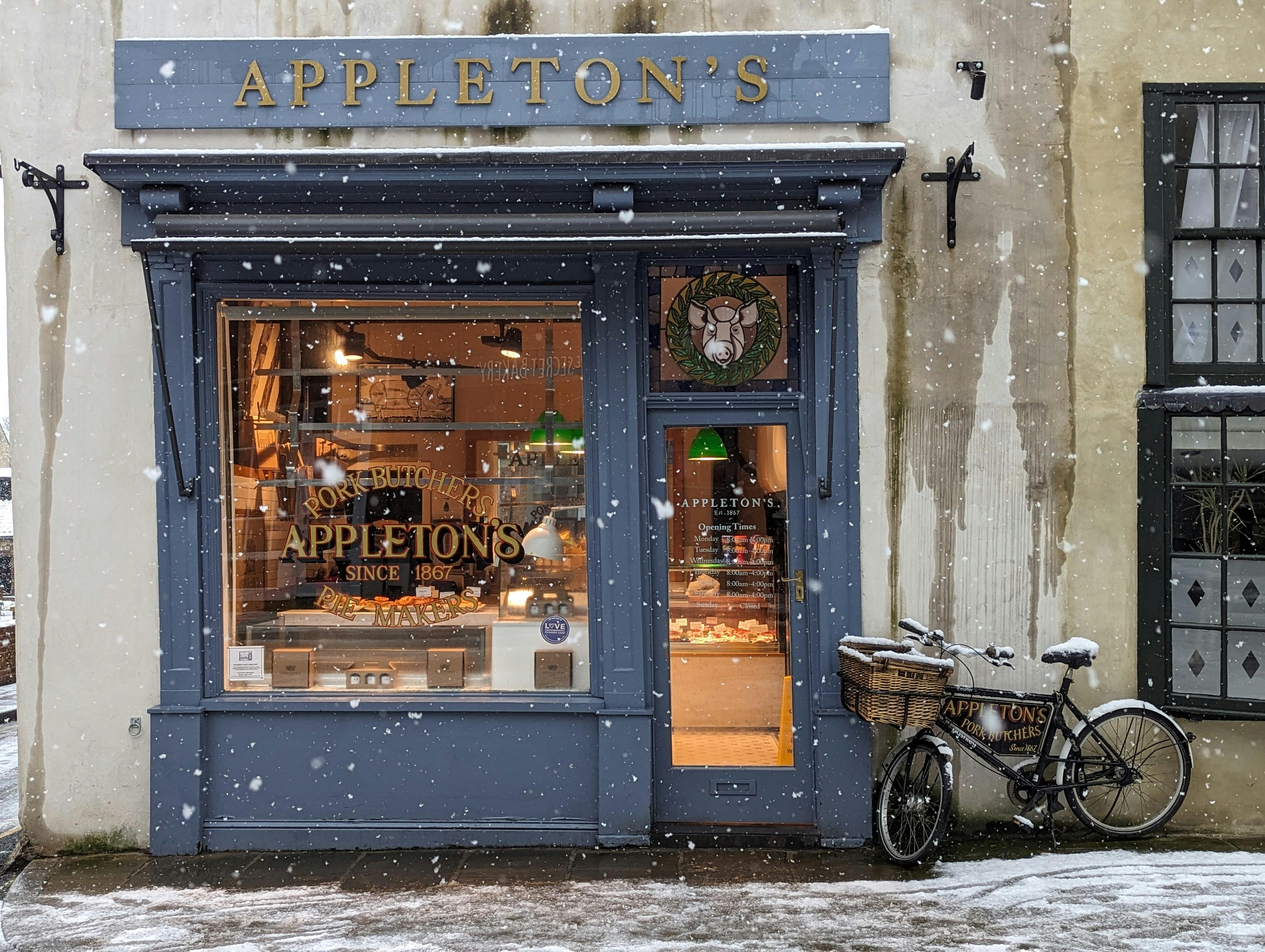 Snowy day at Appleton's butcher shop in Knaresborough, England, showcasing a quaint storefront and delivery bike.