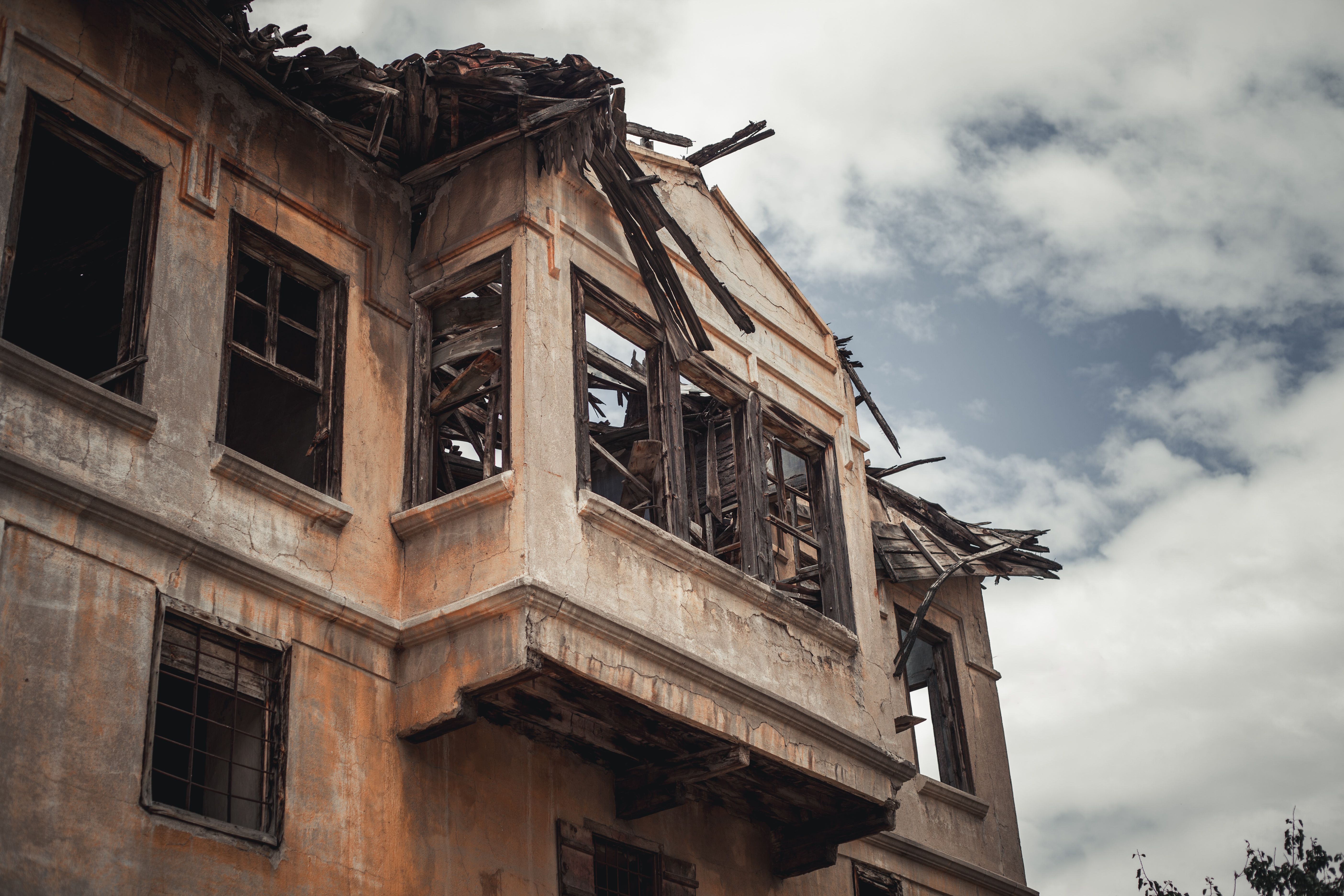 A dramatic view of a dilapidated house with broken windows and a cloudy sky backdrop.