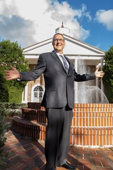 Smiling businessman in suit poses confidently in front of a fountain and classical building.