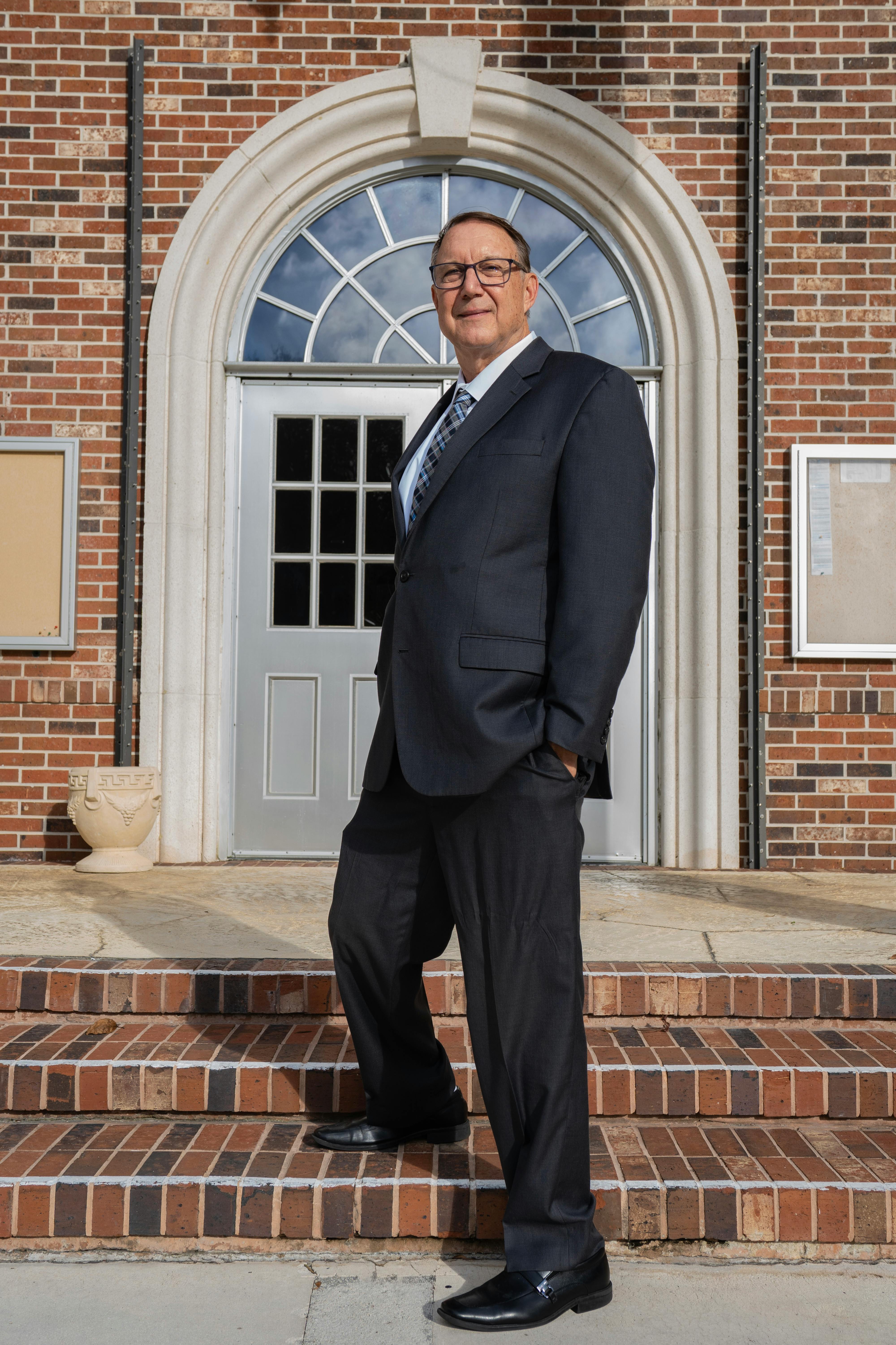 Businessman in a suit standing confidently on brick steps with a historical building doorway in the background.