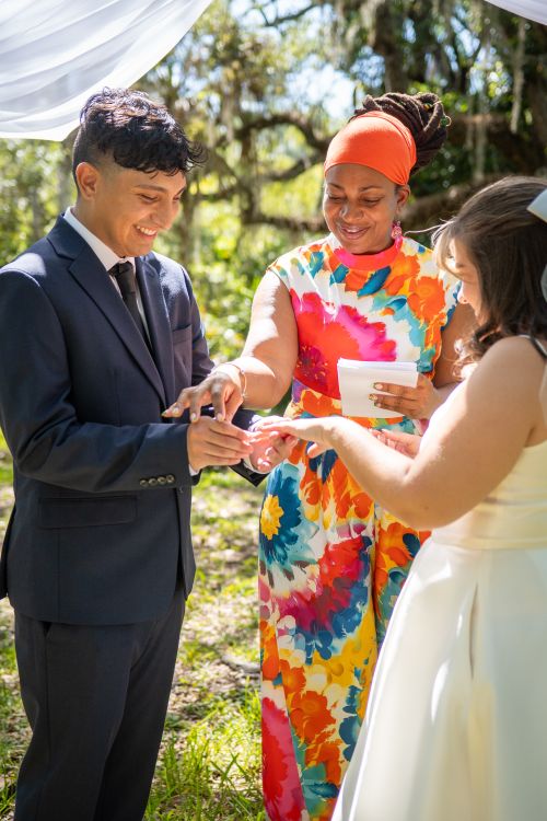 Free A vibrant outdoor wedding with a couple exchanging rings, guided by the celebrant under natural sunlight. Stock Photo
