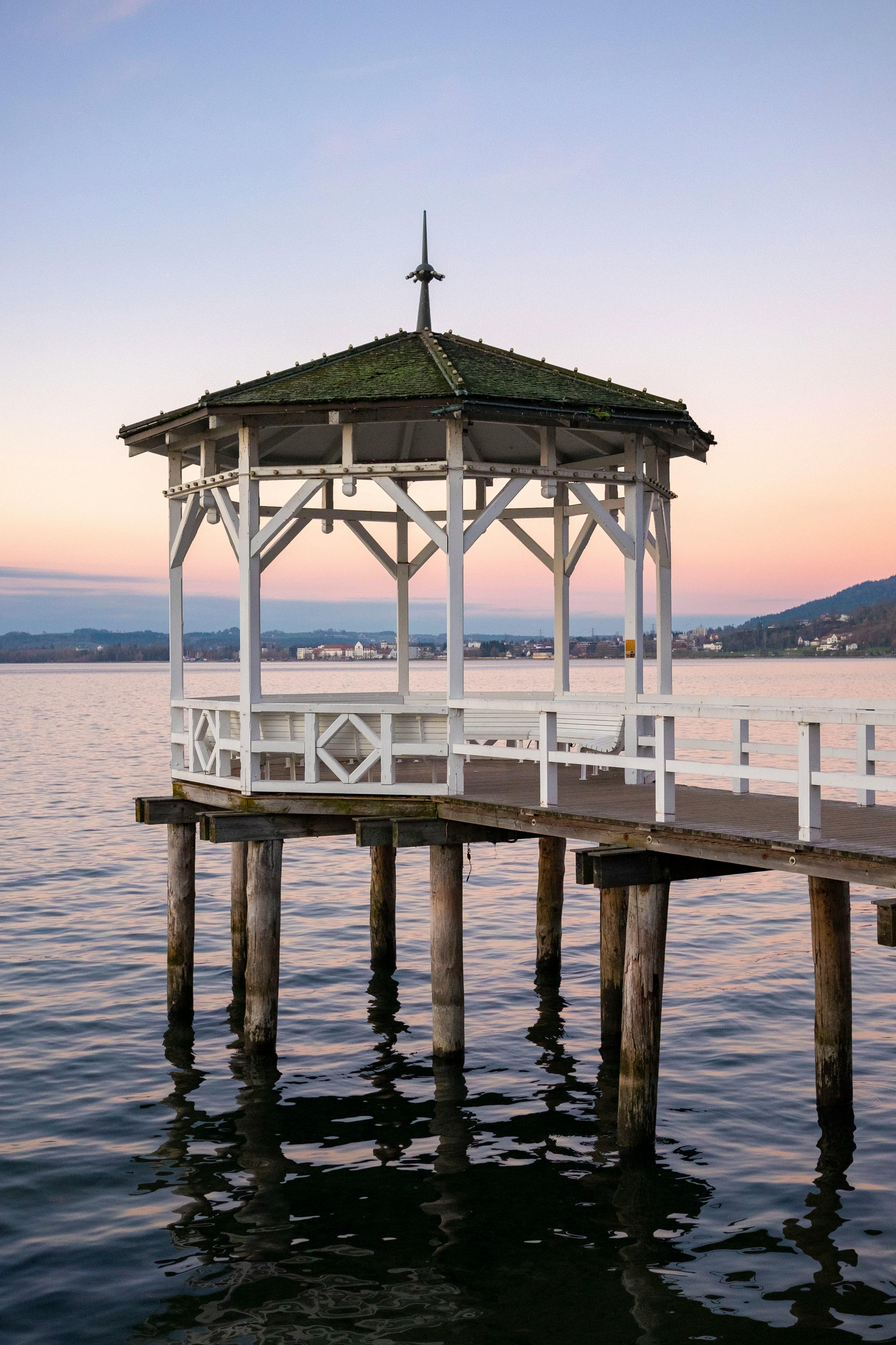 A tranquil white gazebo over calm water during a beautiful sunset.