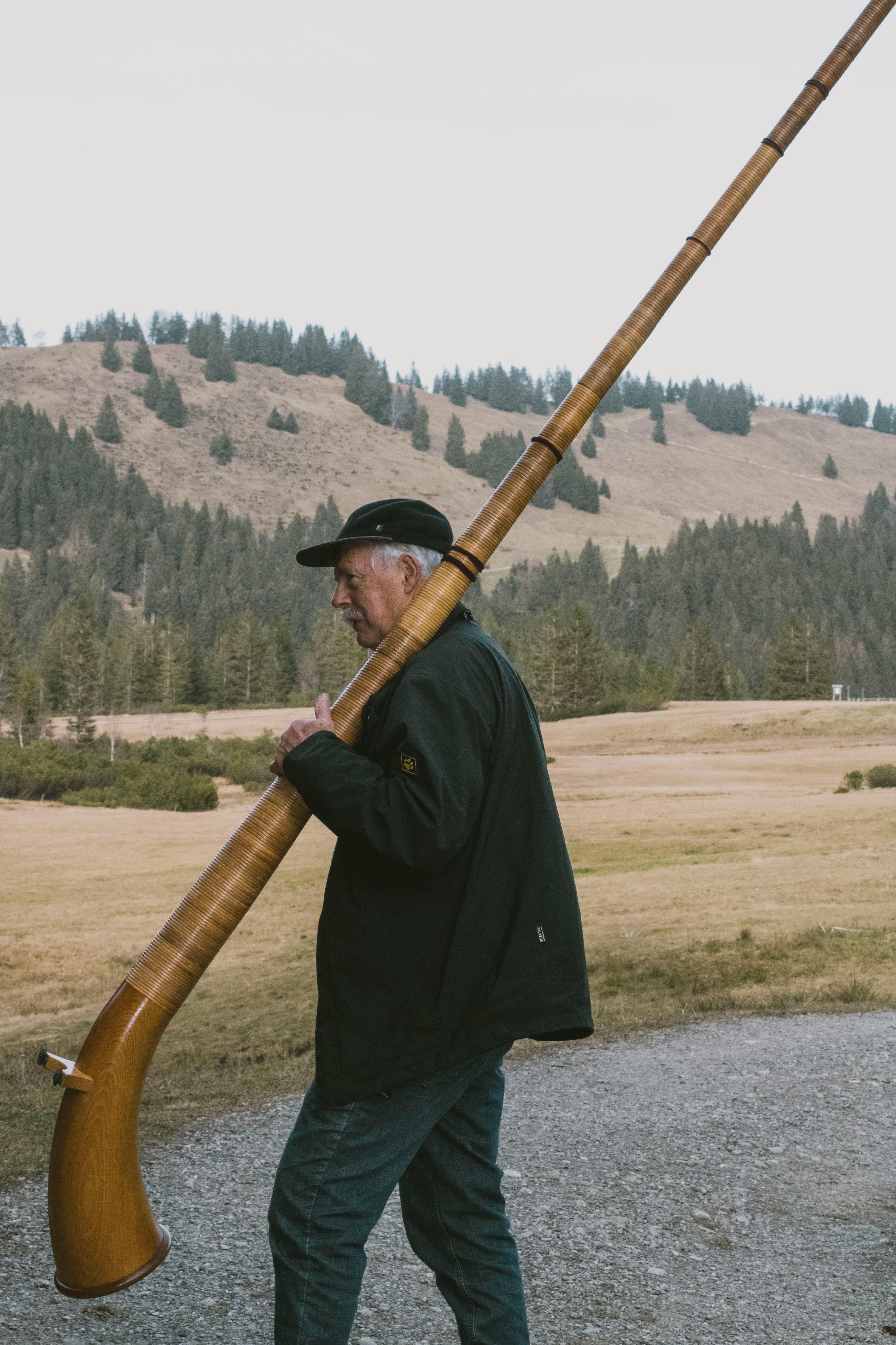 Gratuit Un homme âgé portant un cor des Alpes dans un cadre champêtre pittoresque, évoquant les traditions et la culture musicale. Photos