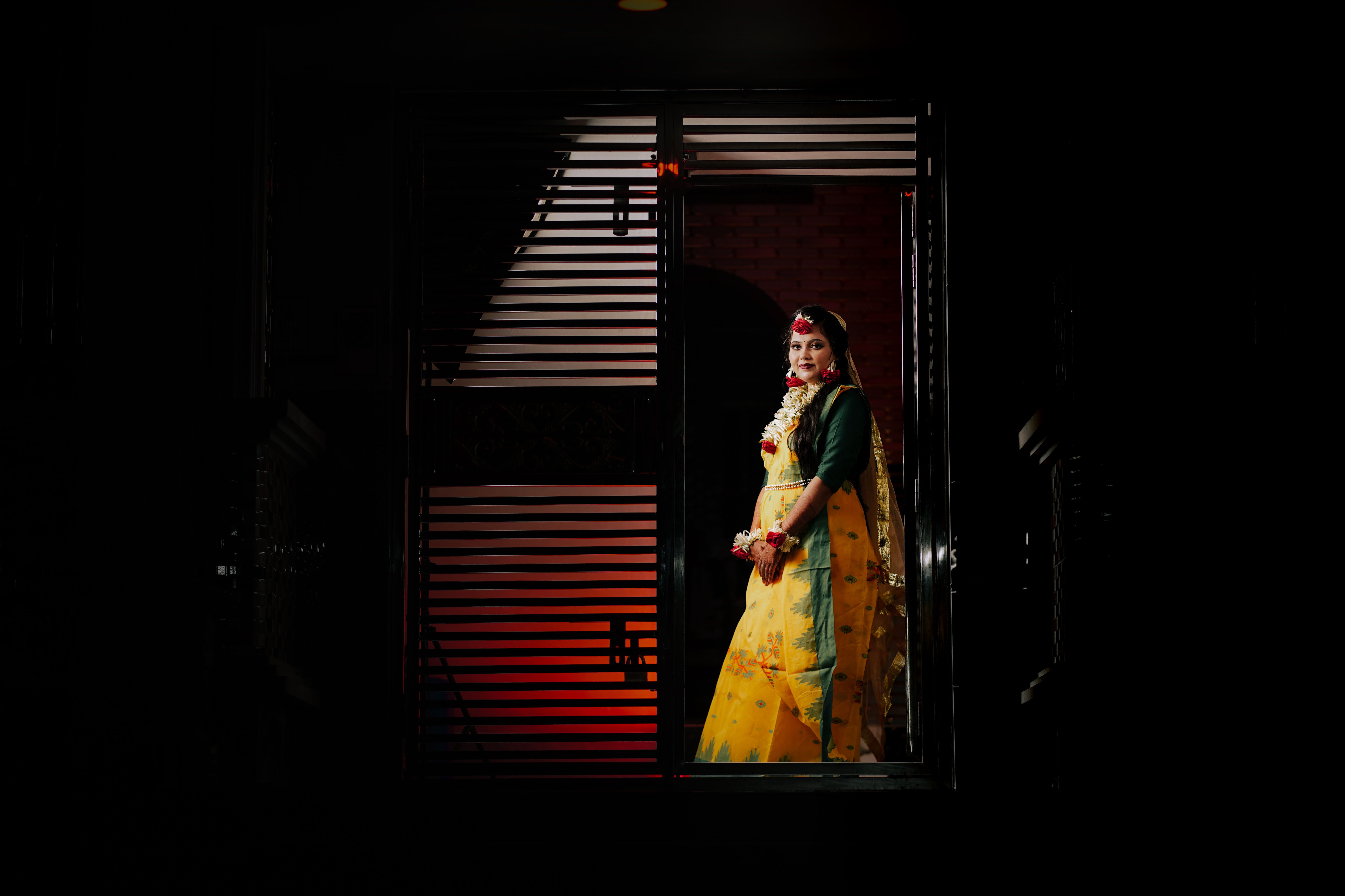 A beautiful woman in traditional attire poses confidently in a doorway with dramatic lighting.