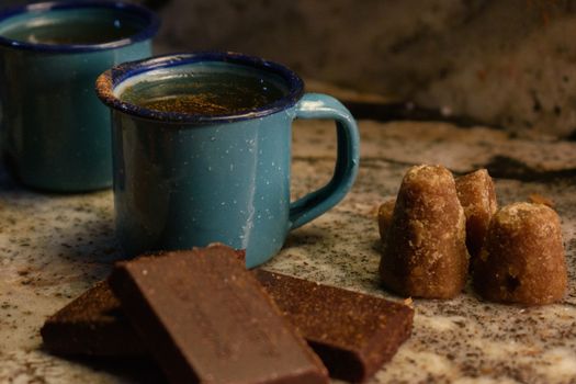 Rustic scene featuring hot chocolate in blue enamel mug, with piloncillo and chocolate blocks on marble.