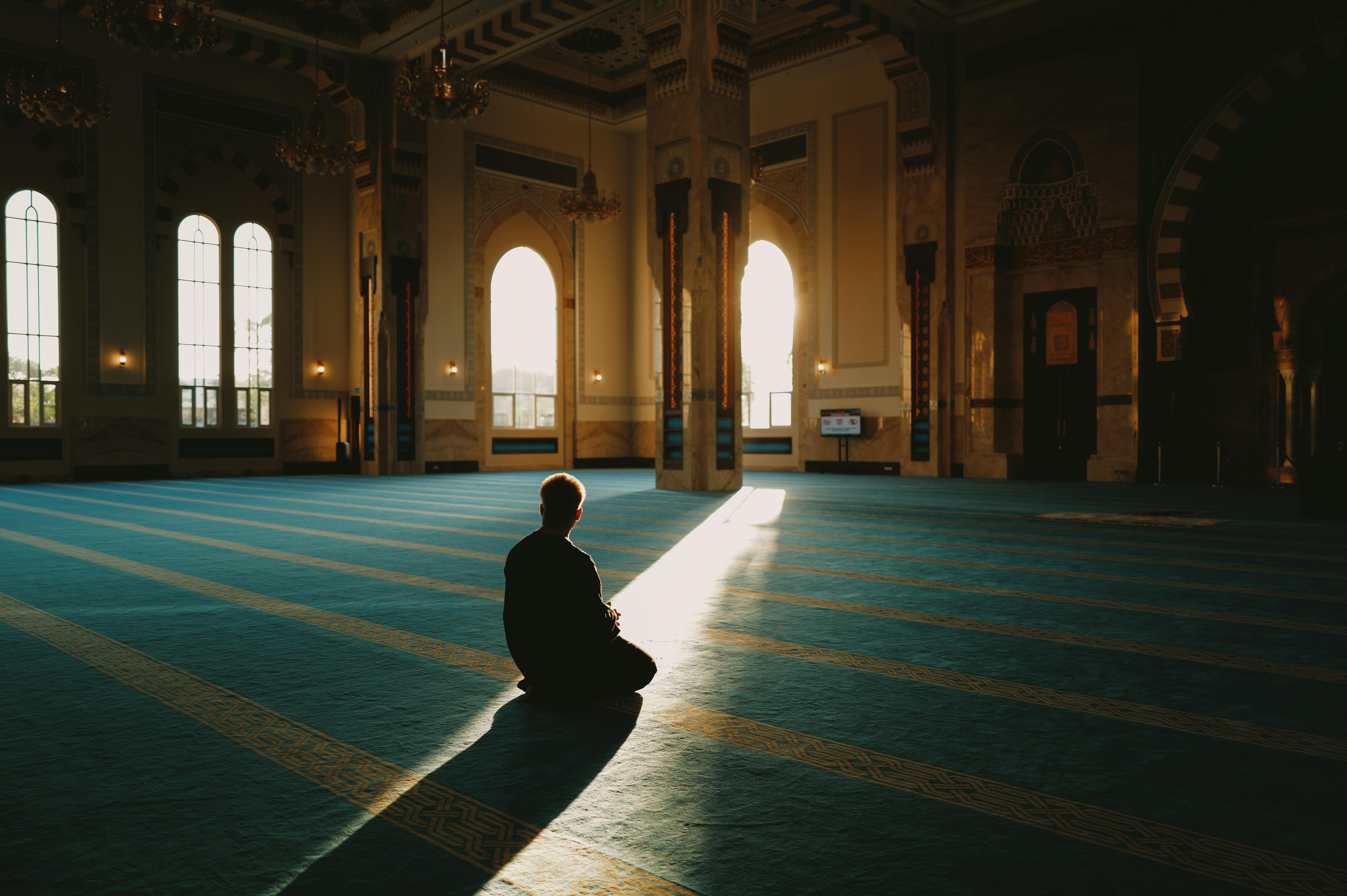 A person in prayer inside Sendayan mosque, illuminated by soft sunlight highlighting the serene architecture.
