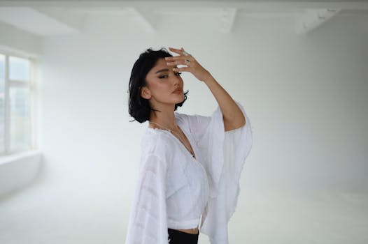 Portrait of a woman in a white dress posing gracefully in a bright minimalist studio.