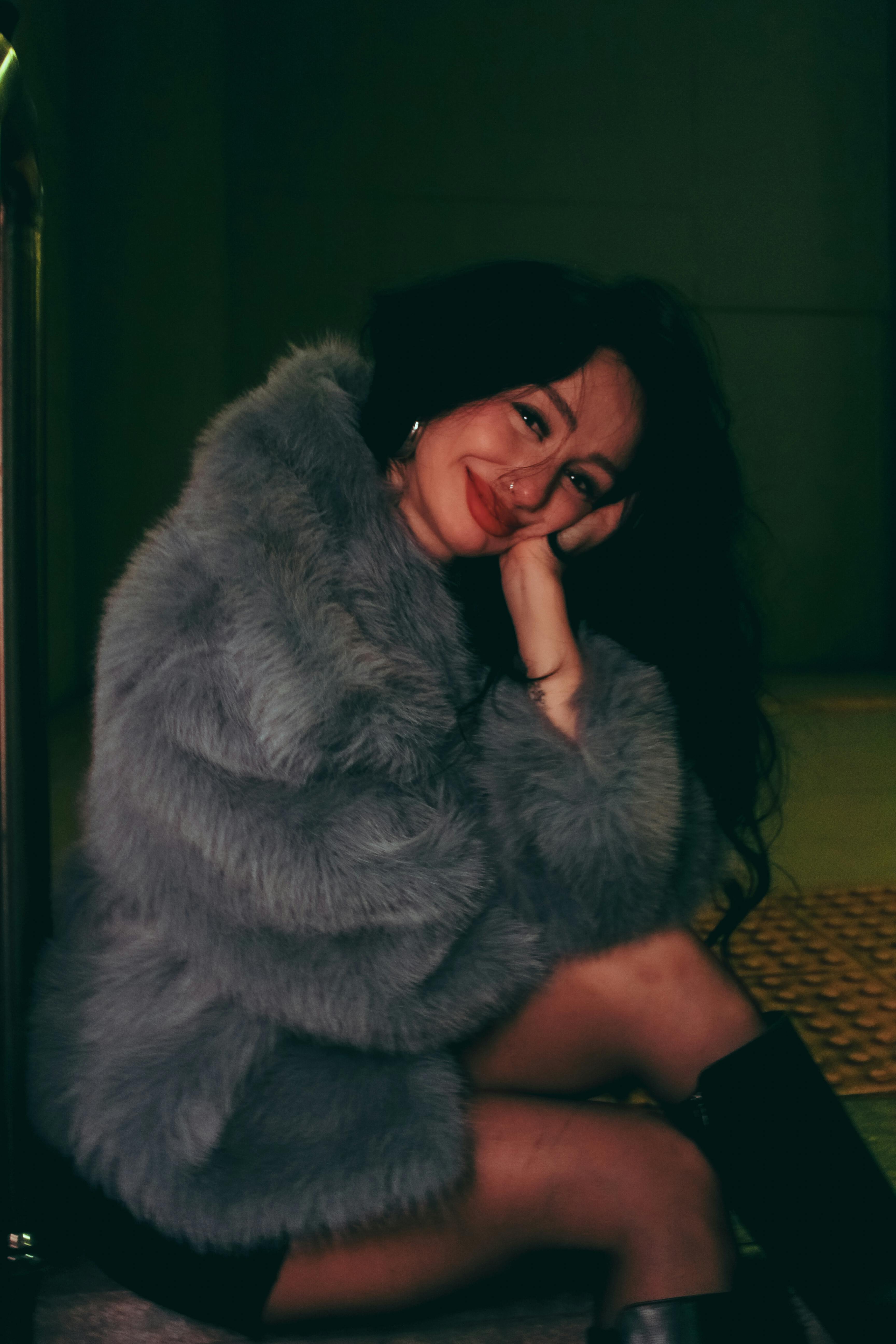 Free Woman in a gray fur coat posing indoors with a smile. Warm and stylish fashion. Stock Photo