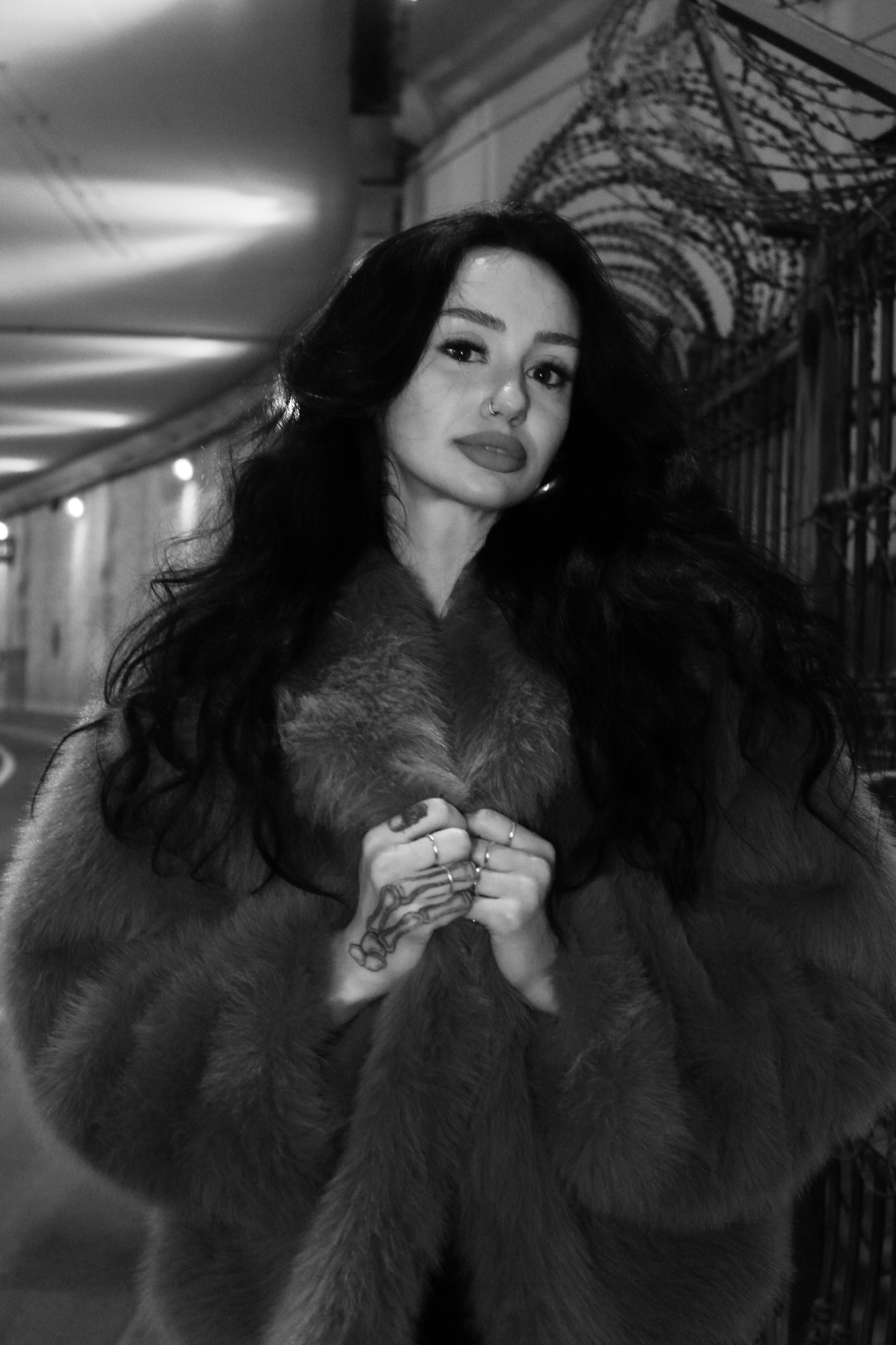 Black and white portrait of a stylish woman in a fur coat at night.