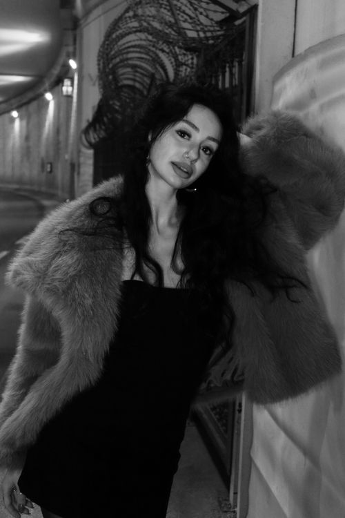 Free Stylish black-and-white portrait of a woman wearing a fur coat posing in an urban setting at night. Stock Photo