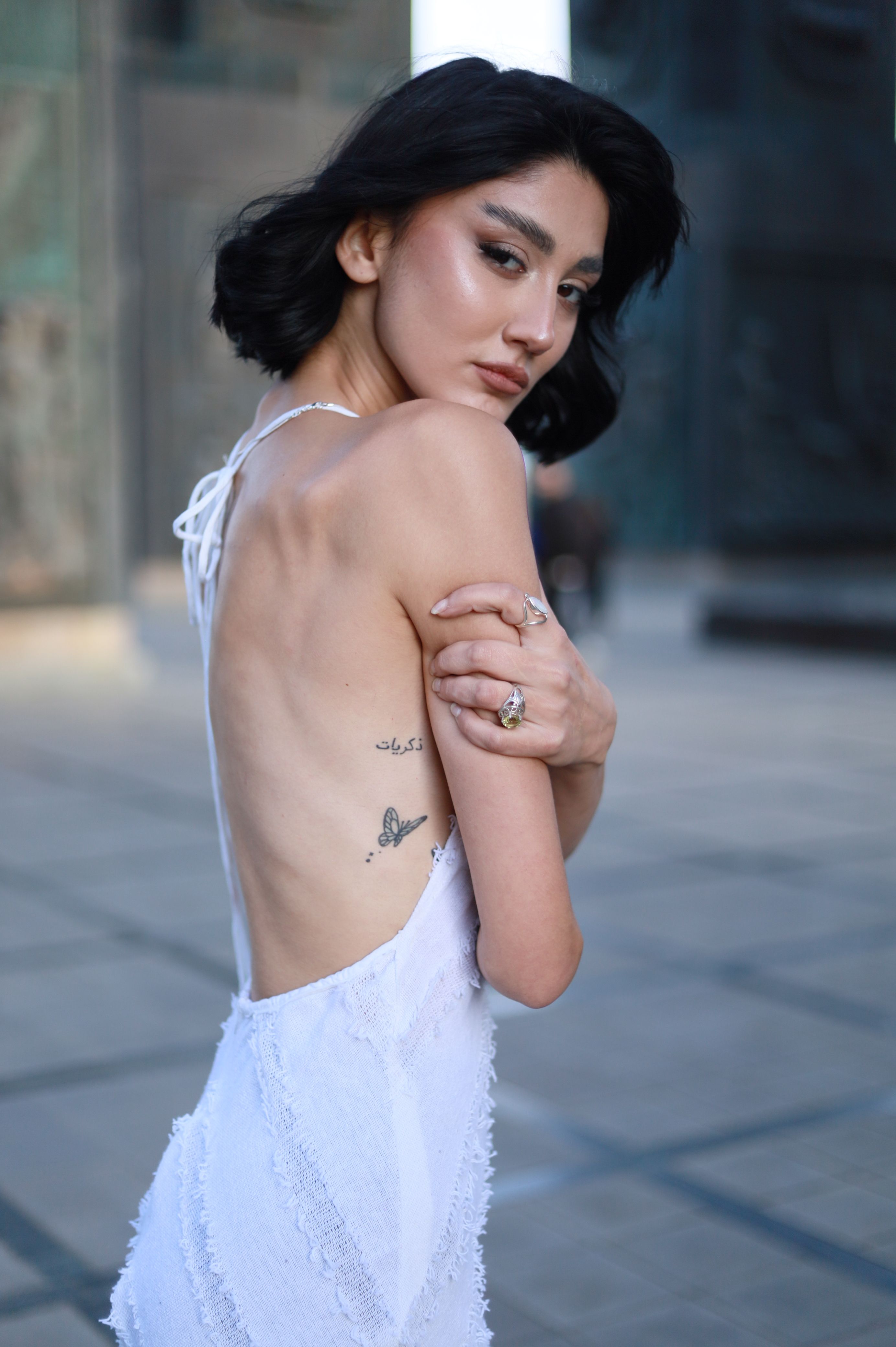 Artistic outdoor portrait of a woman in a white dress displaying a butterfly tattoo.
