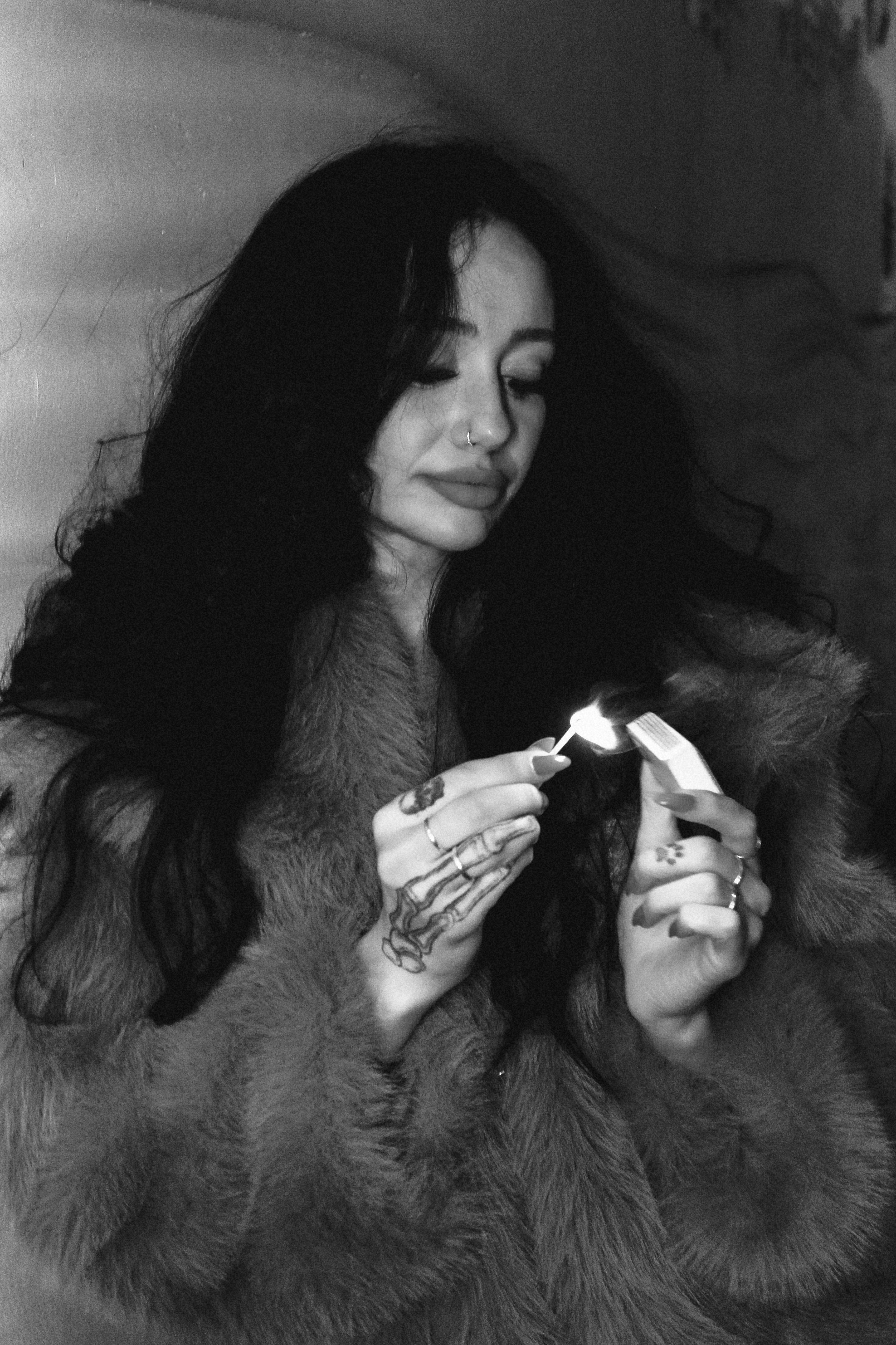 Dramatic black and white photo of woman with tattoos lighting a match.