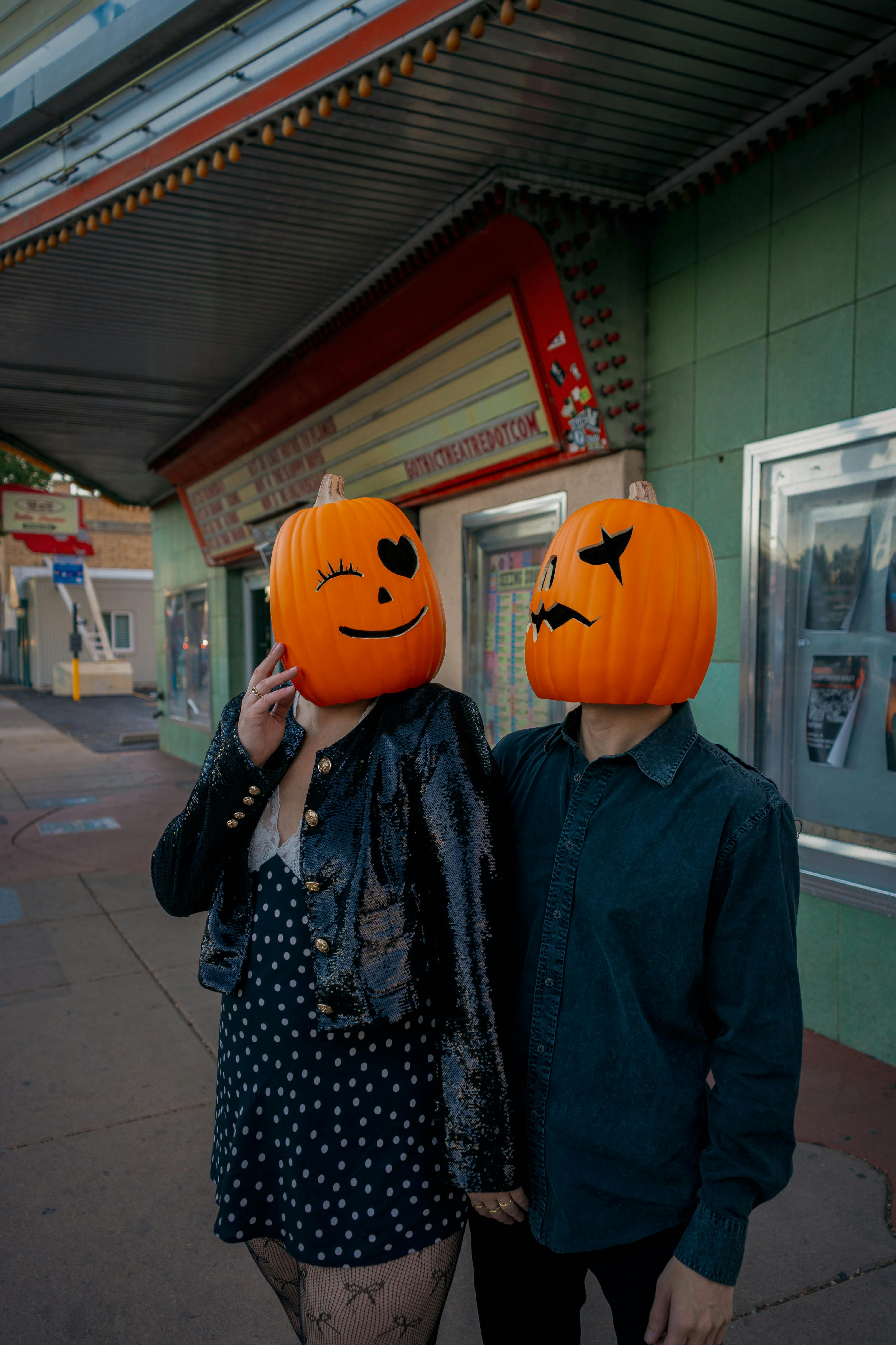 Ücretsiz Englewood'daki bir tiyatronun dışında oyulmuş balkabağı kafalarıyla poz veren bir çift, sonbahar havasını yansıtıyor. Stok Fotoğraflar