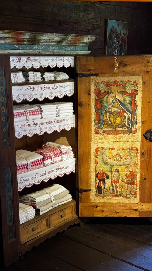 Free Antique wooden cupboard filled with neatly folded linens and adorned with historical artwork. Stock Photo