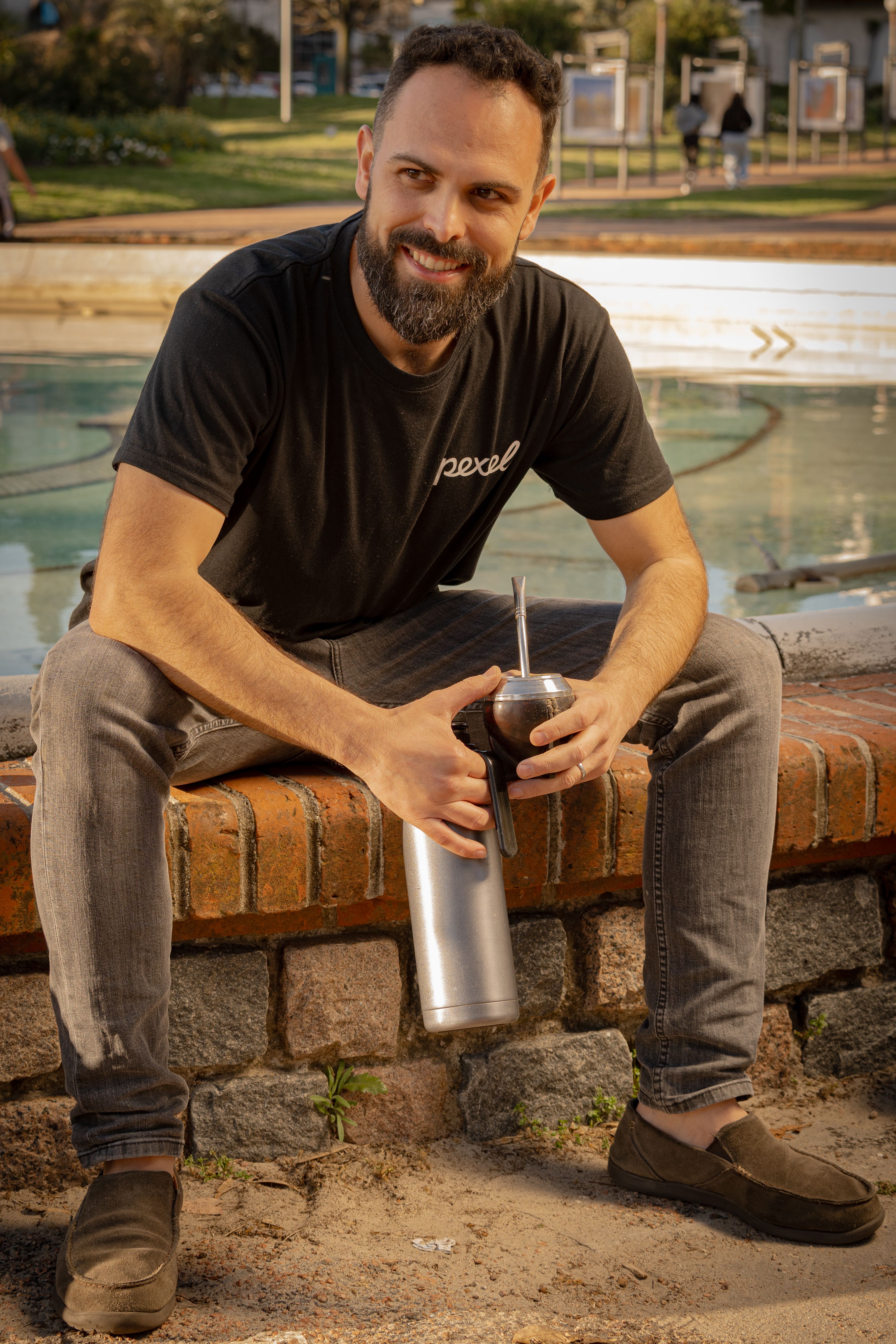 A man sitting by a fountain in Montevideo, enjoying a traditional yerba mate drink.
