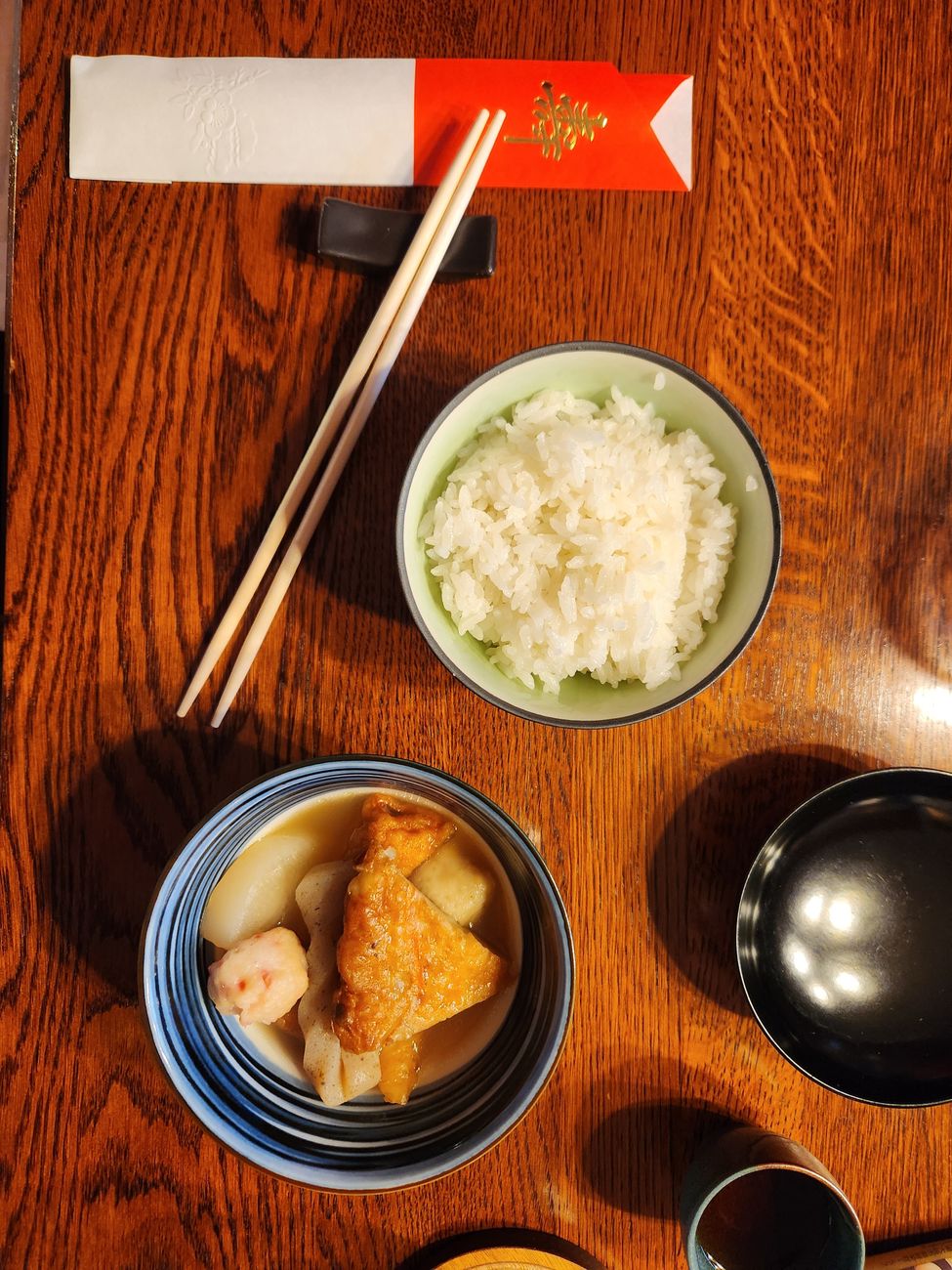 A generous bowl of Sichuan fish and tofu stew showing chunks of flaky white fish and golden tofu cubes in a rich, reddish-brown sauce, topped with bright green scallions and served with a bowl of steamed rice