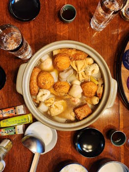 A top-down view of a traditional Japanese oden dish in a clay pot, surrounded by dining utensils.