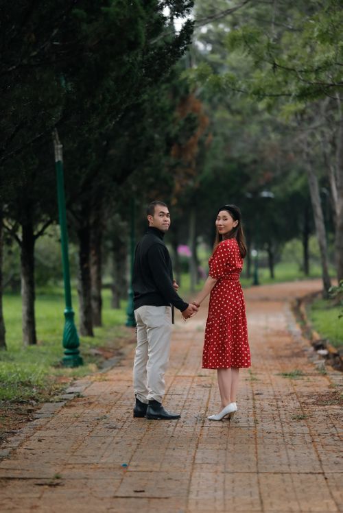 Free A couple holds hands while walking on a scenic park pathway surrounded by trees. Stock Photo