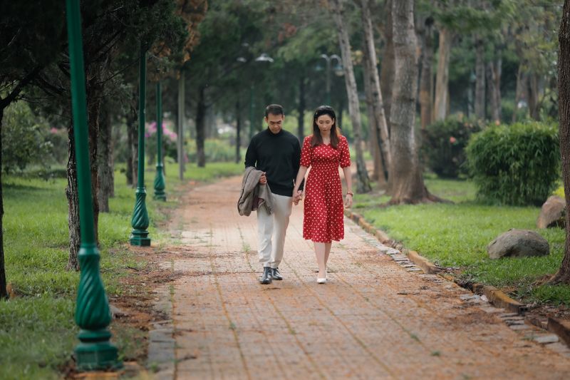 A couple walks hand in hand along a scenic park pathway surrounded by greenery.