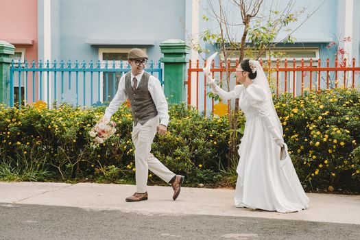 Bride and groom in playful pose on colorful urban street backdrop.