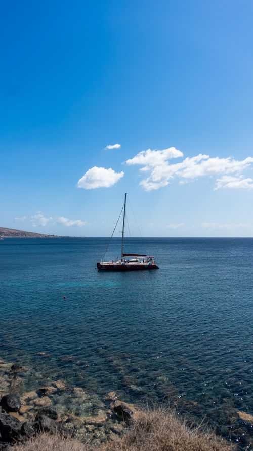 Free A tranquil scene featuring a lone sailboat on crystal clear ocean waters under a bright blue sky. Stock Photo