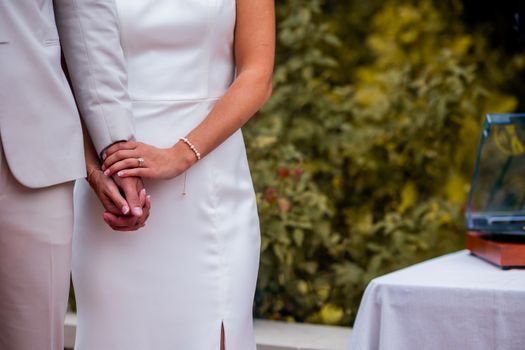A bride and groom elegantly hold hands at an outdoor wedding ceremony, symbolizing unity and love.