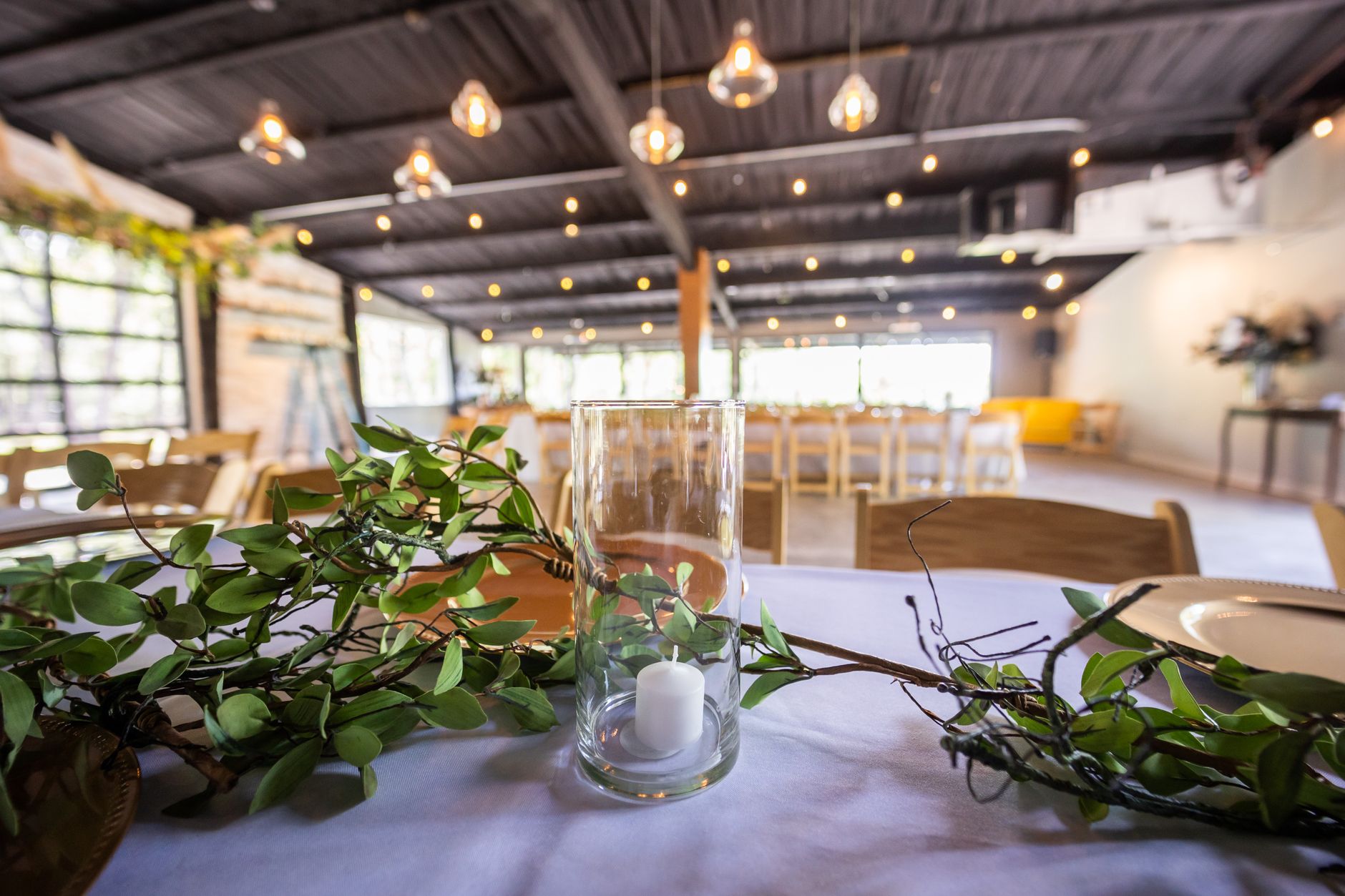 Stylish event venue with glass candle holder and greenery in focus, perfect for weddings or receptions.