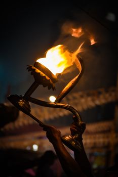 Dramatic photo of hands holding a flaming torch against a dark night sky, evoking a sense of tradition and celebration.