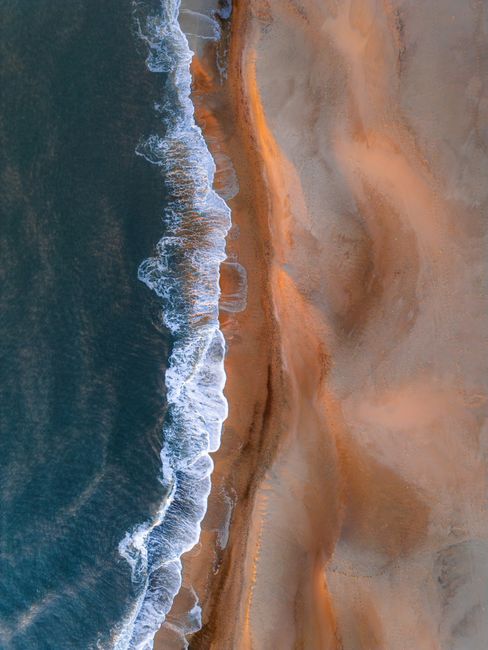 Stunning aerial photo of a sandy beach and ocean waves at sunset along the Danish coastline.