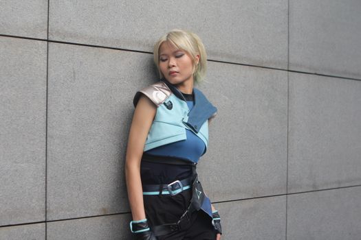 A person in futuristic cosplay leans against a modern concrete wall.