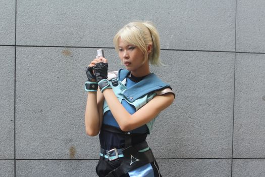 Cosplayer dressed in a futuristic outfit poses against a gray wall outdoors, exuding a sci-fi style.