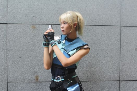 Young woman in futuristic cosplay outfit holding a blaster, posing against a neutral background.